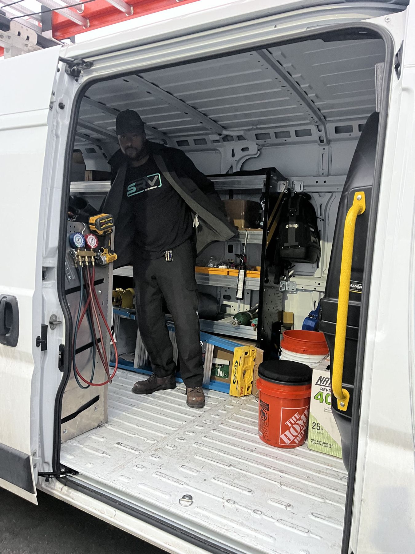 SRV technician standing in the back of a stocked SRV service van with manifold gauges, ladders, refrigerant and tools racked around him