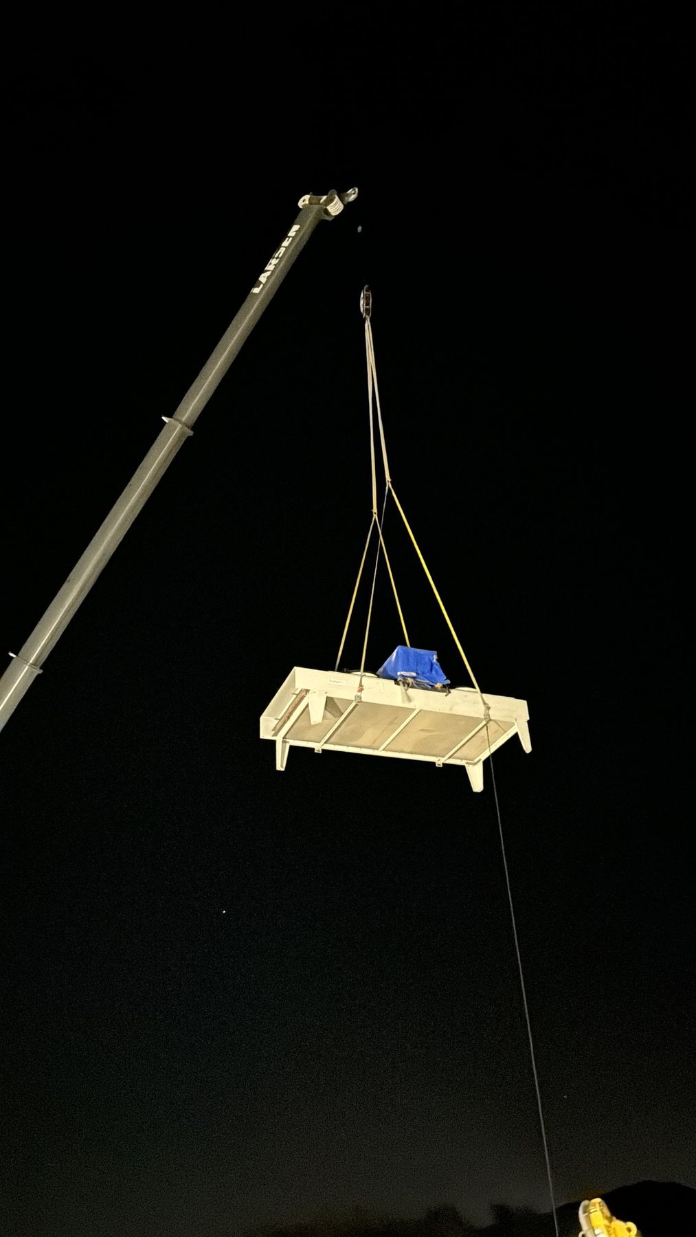 Crane lifting a piece of commercial equipment on a rigging platform against a night sky during an SRV project set