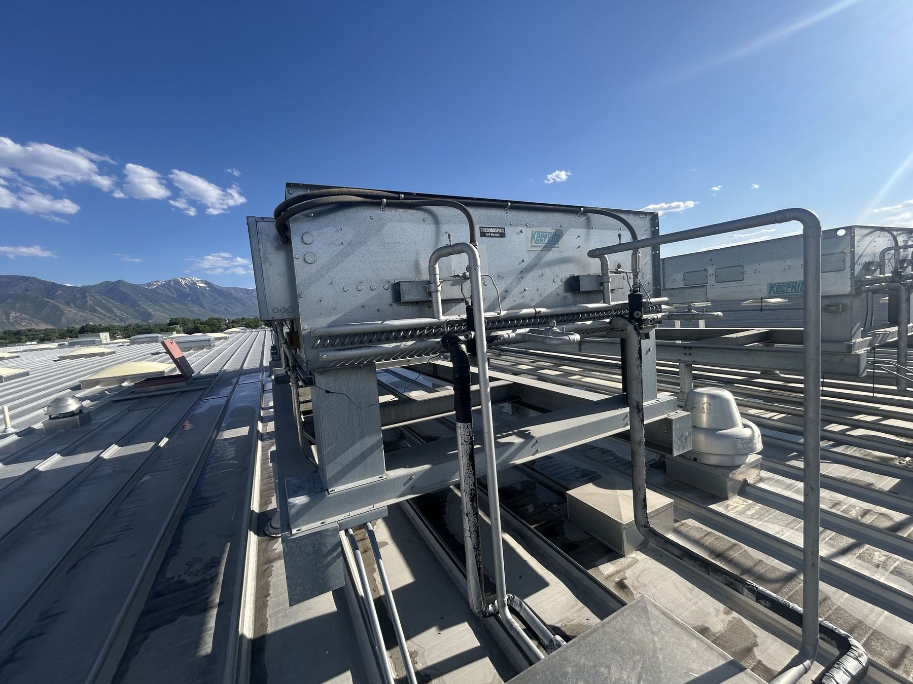 Rooftop refrigeration condenser and piping on a large commercial building in Utah County, with the Wasatch range behind it